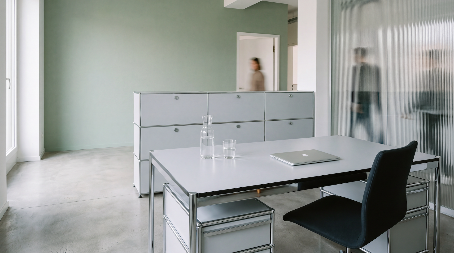 Ruhiges Büro mit Schreibtisch, Laptop und einer Person hinter einer Riffelglaswand