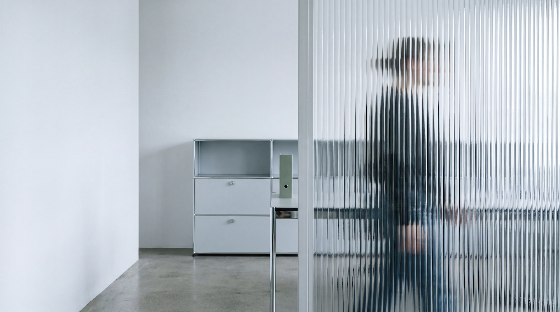 Ruhiges Büro mit Sideboard und einer Person hinter einer Riffelglaswand